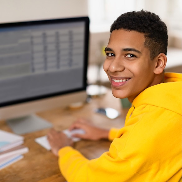 student smiling at camera while working on computer
