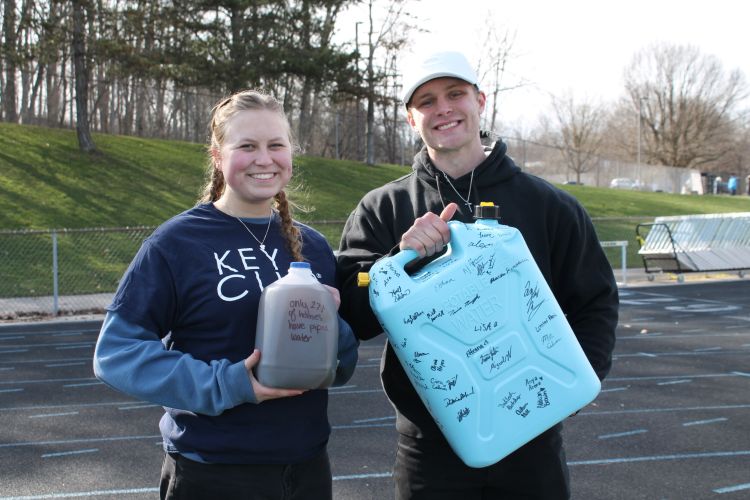 Maddy and another student holding gallon jugs standing on a track