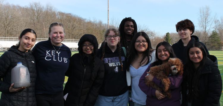 Students posing together on a field with one of them holding a dog
