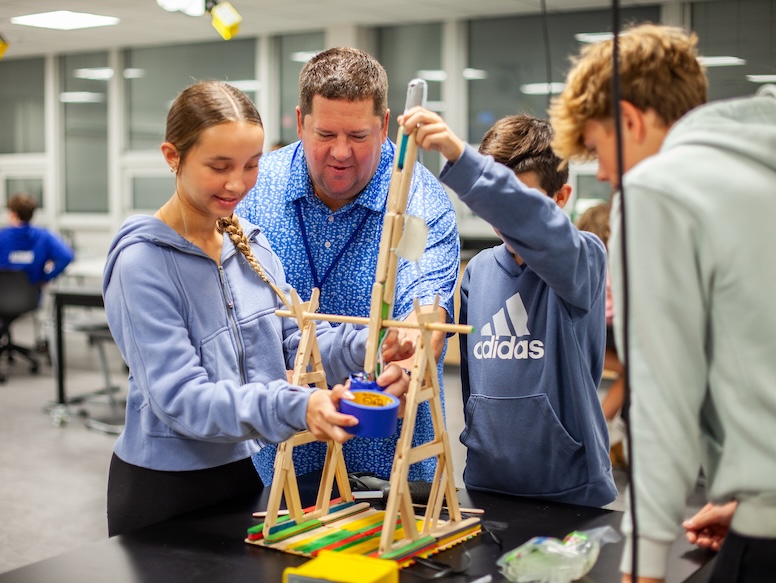 Teacher helping students build a contraption out of popsicle sticks and tape
