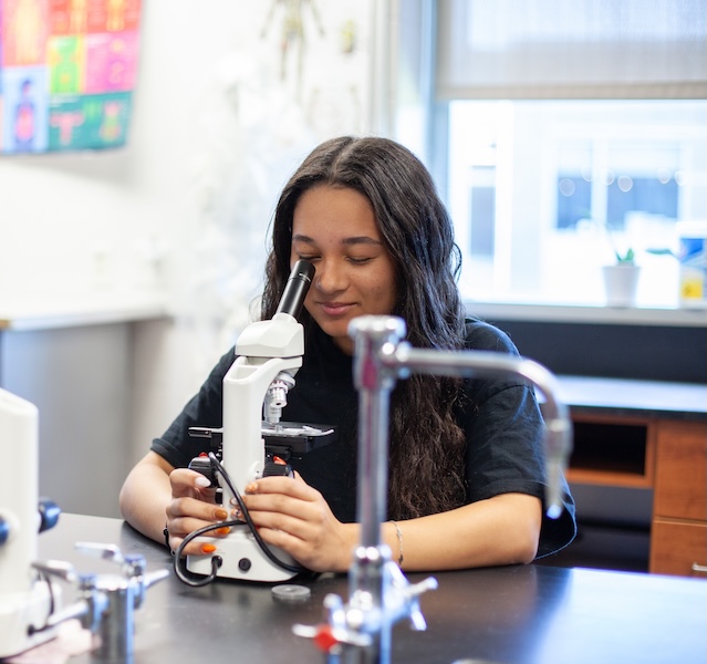 female student using a microscope to analyze something