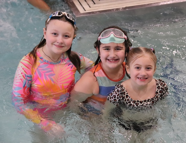 three young female students posing for a picture while swimming in a pool