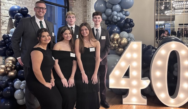 students and a staff member posing next to a large illuminated 40 sign
