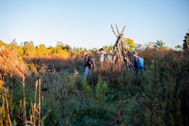 student walking through fields with a teepee in the background